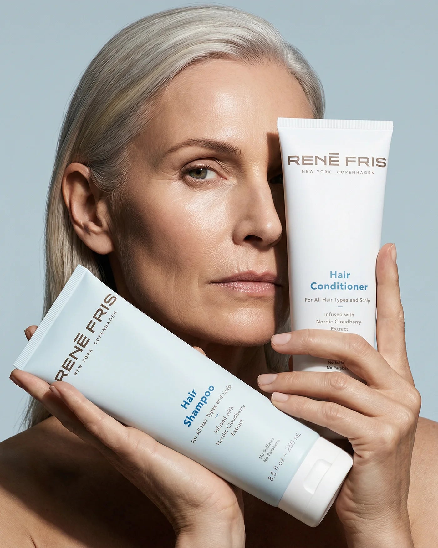 Woman holding Rene Fris Hair Shampoo and Hair Conditioner bottles against a light blue background