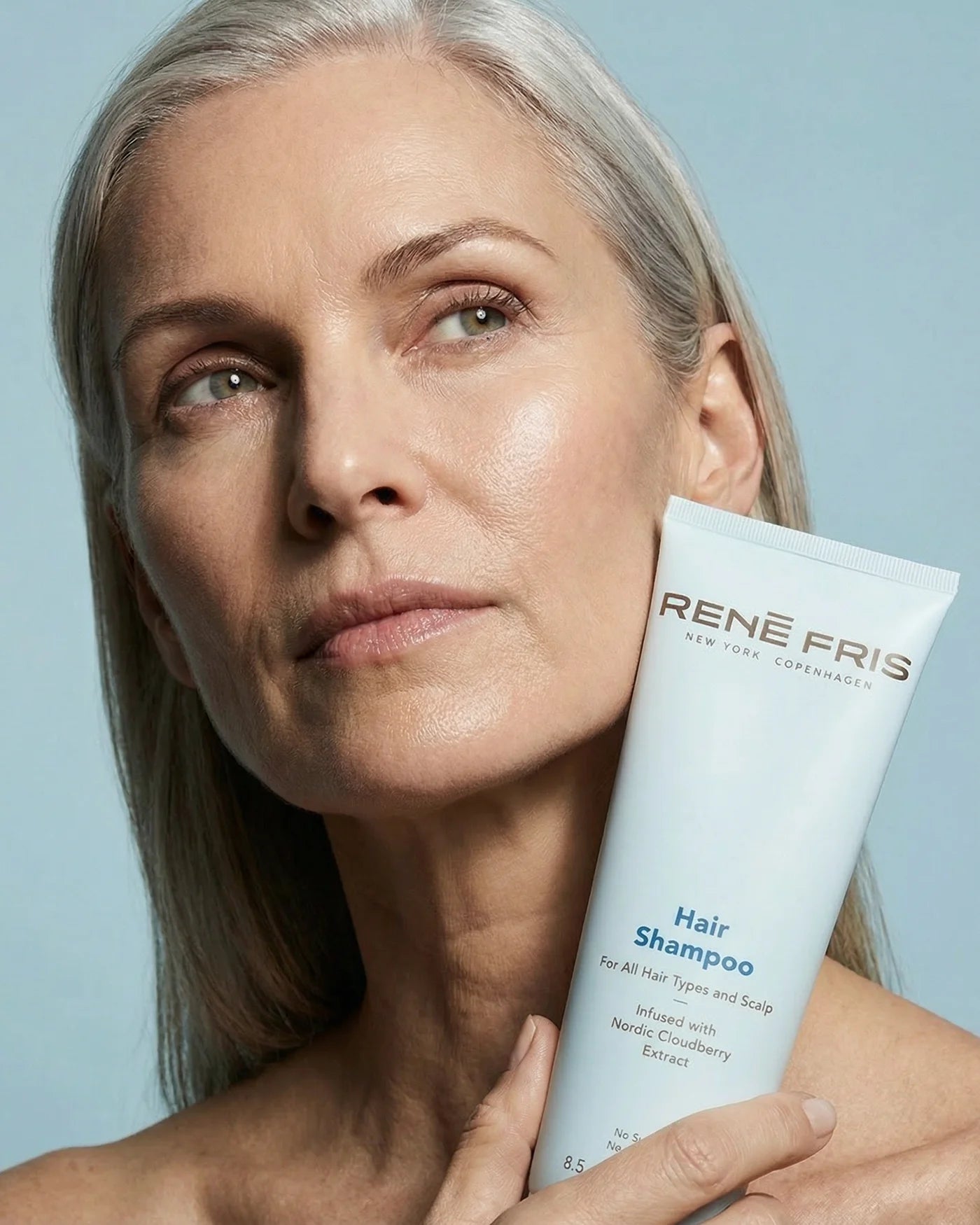 Woman holding a Rene Fris hair shampoo tube against a light blue background