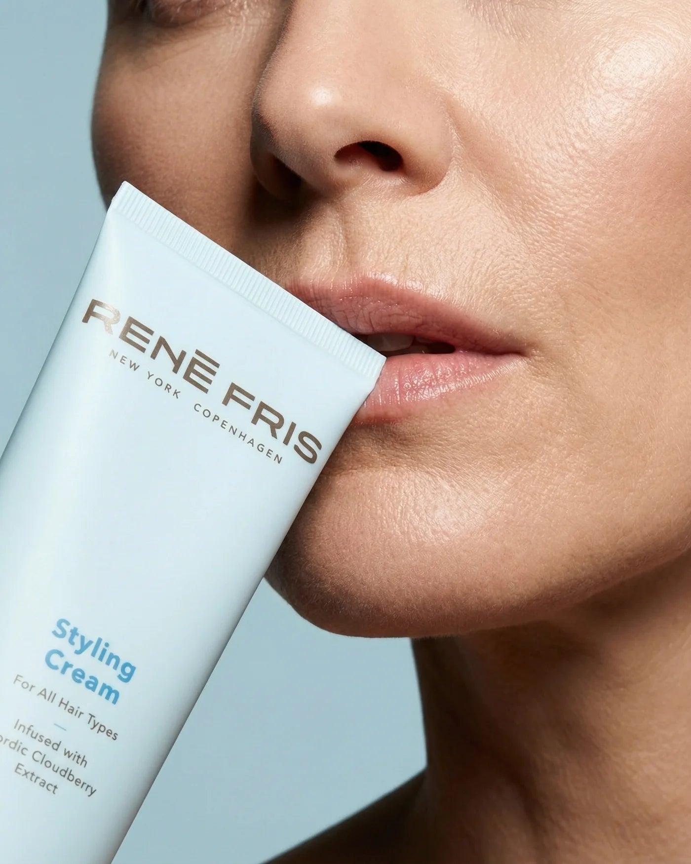 Close-up of a person holding a Rene Fris styling cream can near their face against a light blue background