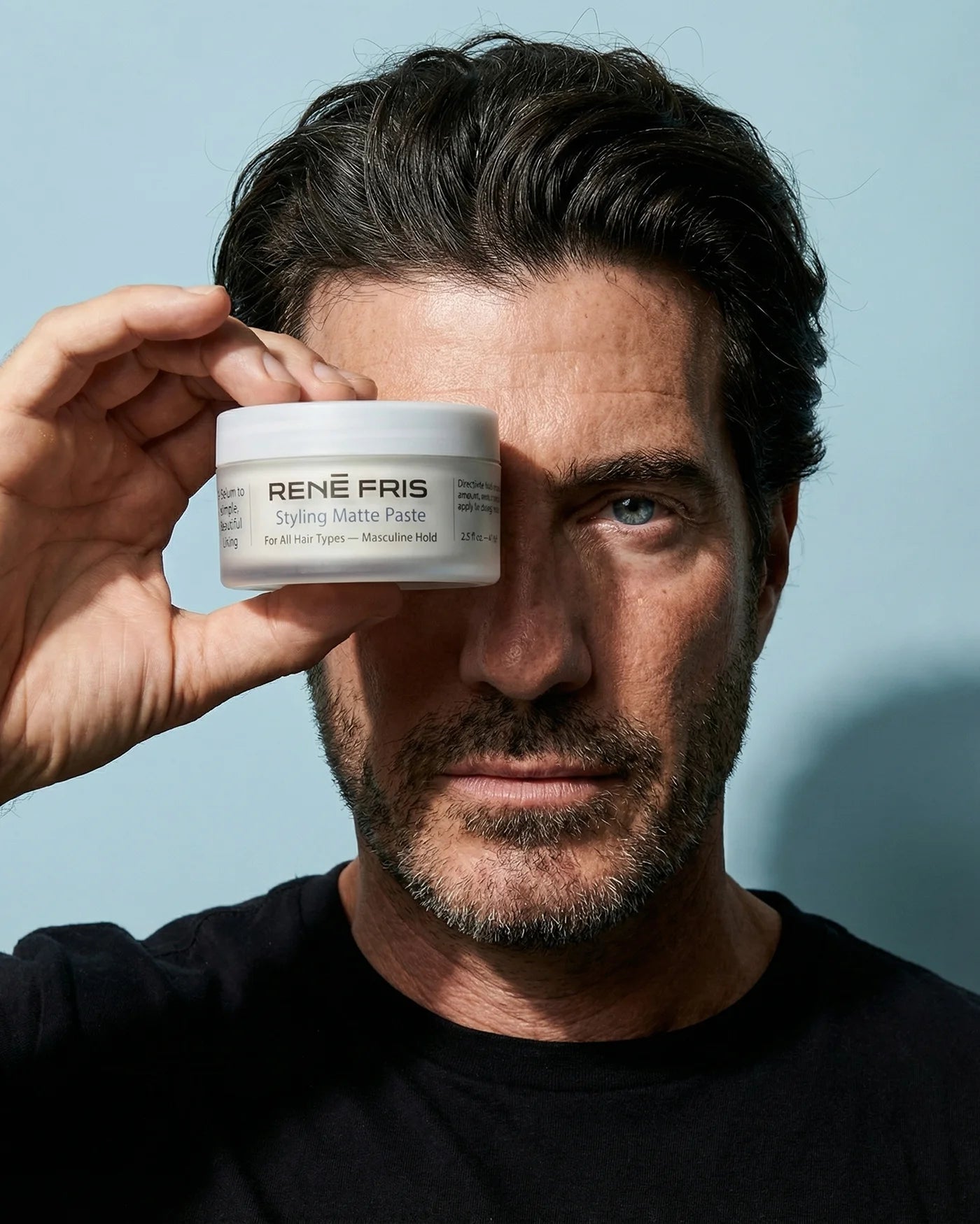René Fris holding a jar of René Fris styling matte paste against a light blue background