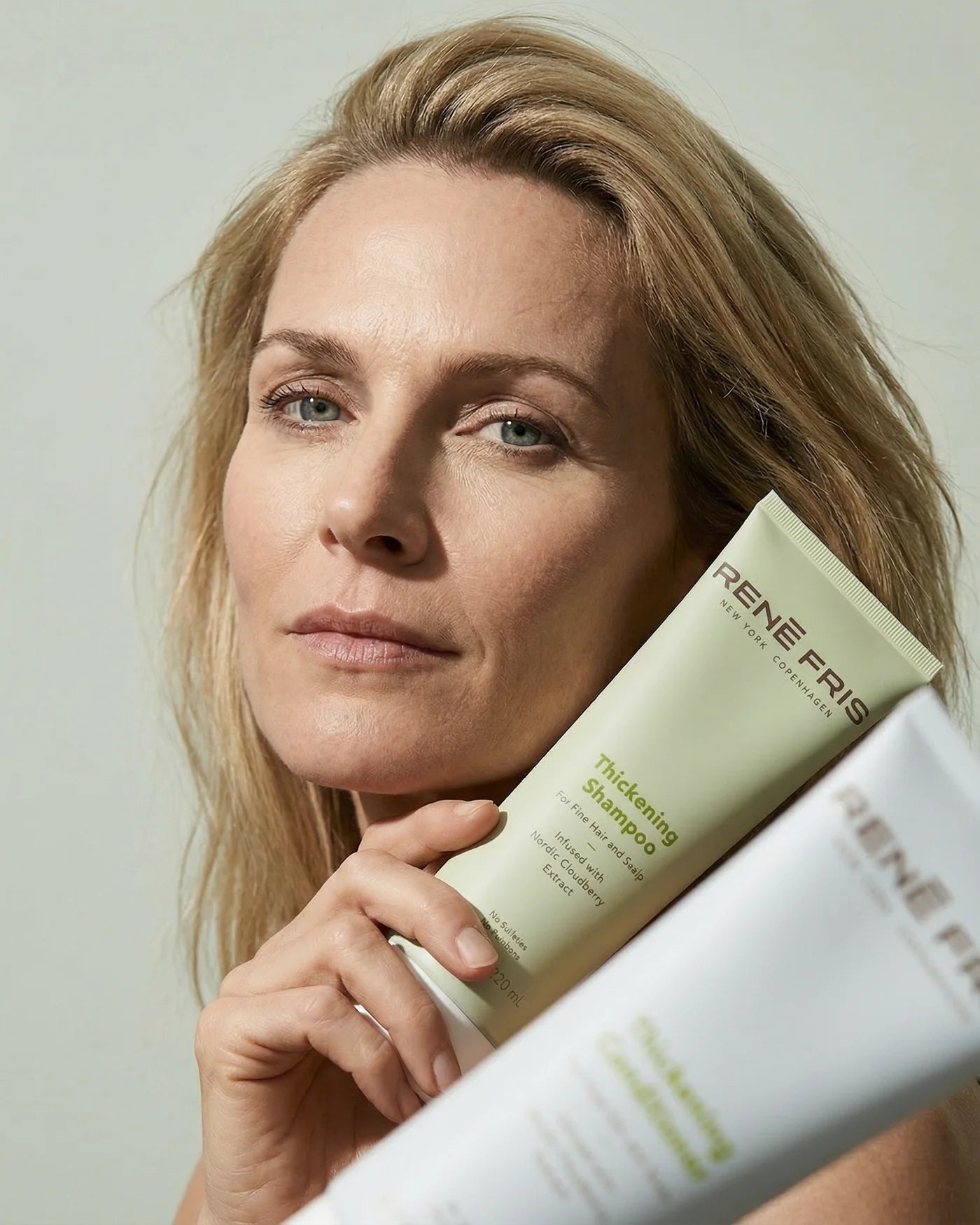 Woman holding a tube of Rene Fris shampoo and conditioner against a plain background