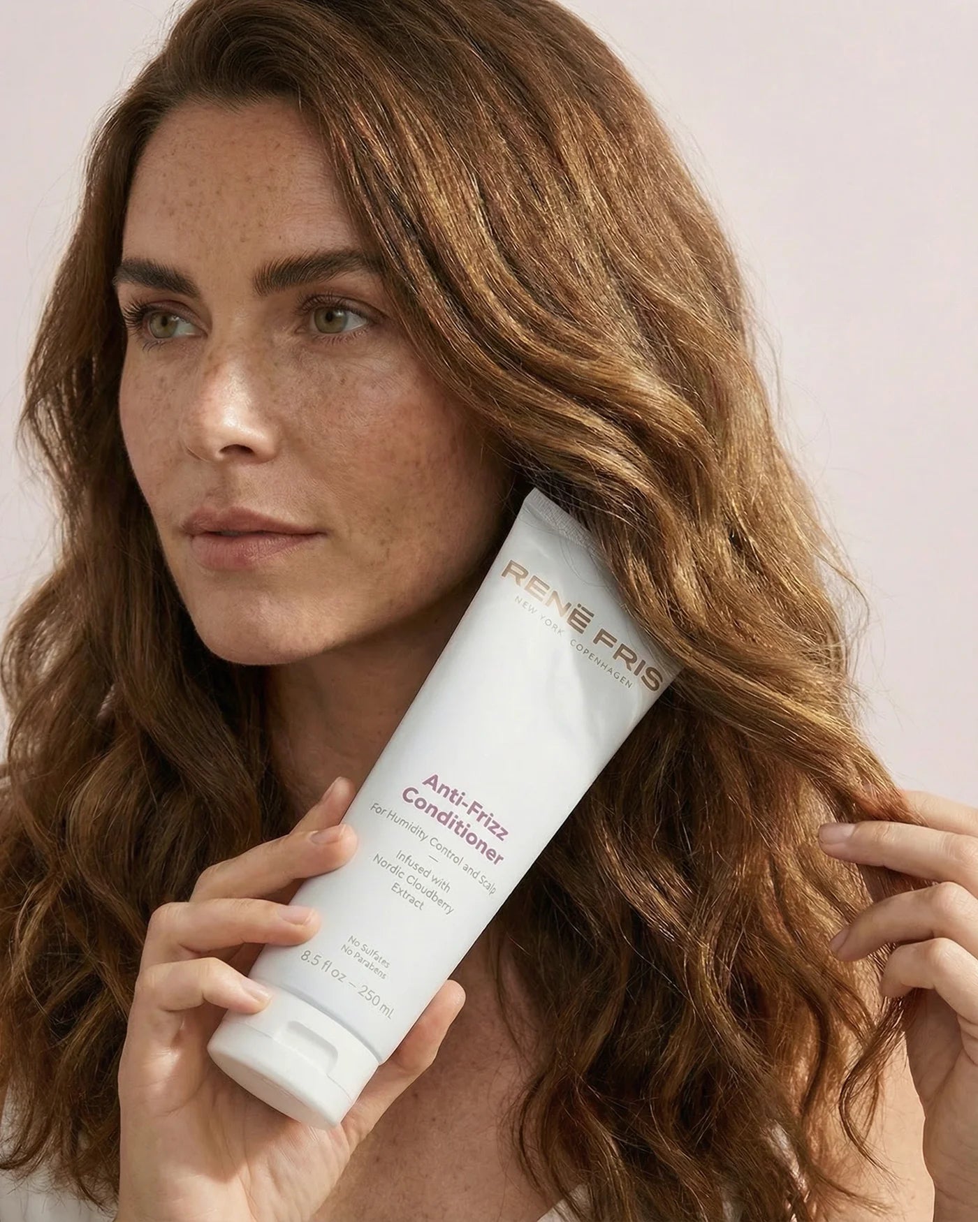 Woman holding a bottle of René Fris Anti-Frizz Conditioner with a neutral background