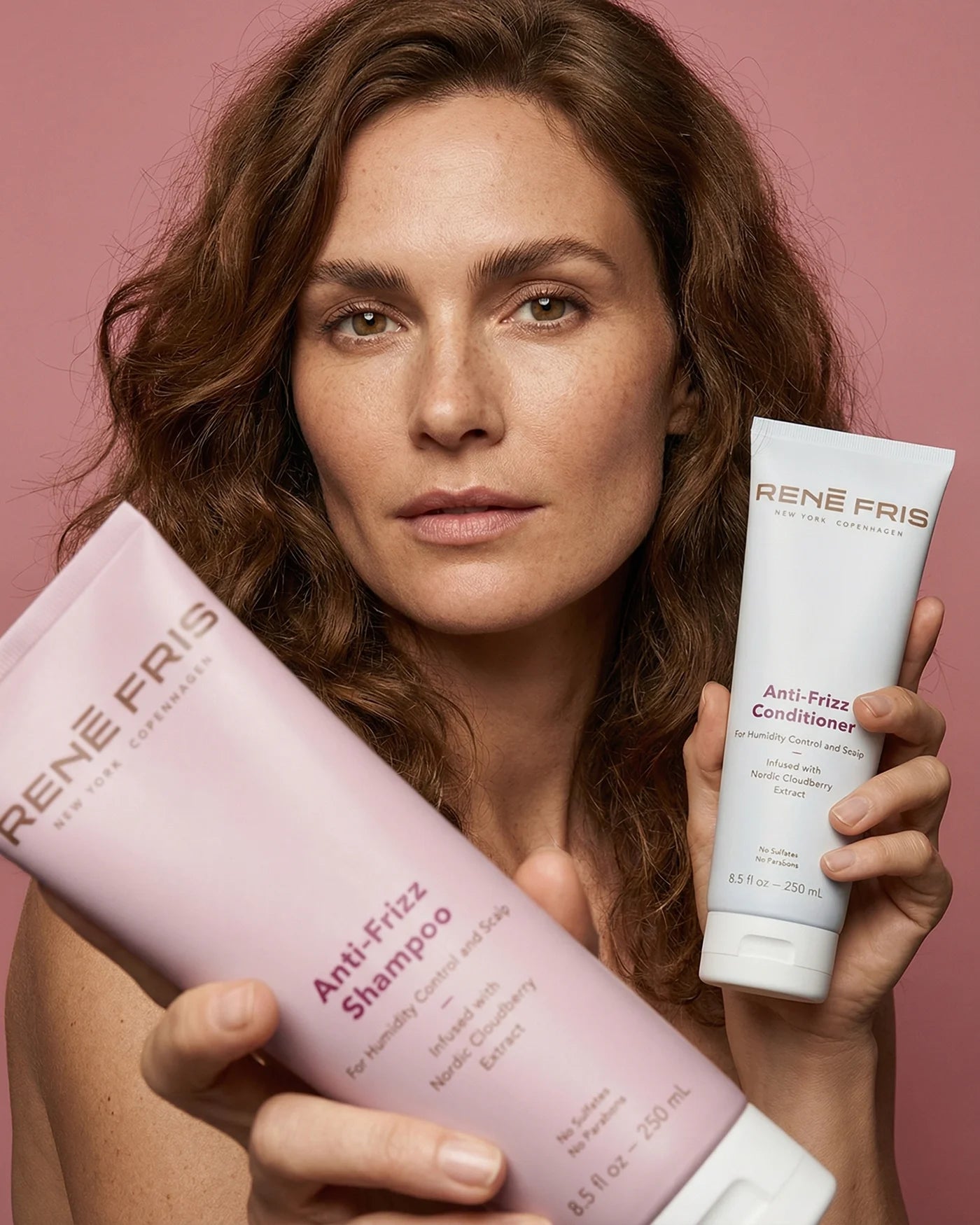 Woman holding René Fris Anti-Frizz shampoo and Anti-Frizz conditioner against a pink background