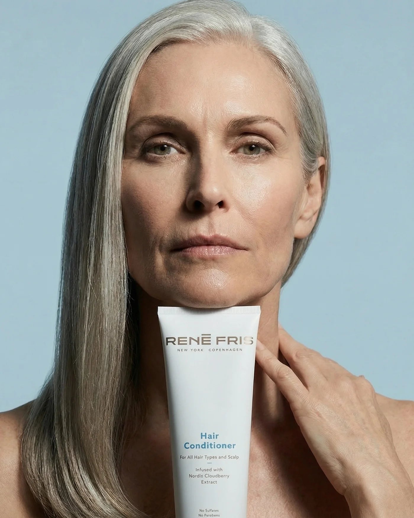 Woman holding a Rene Fries hair conditioner tube against a light blue background