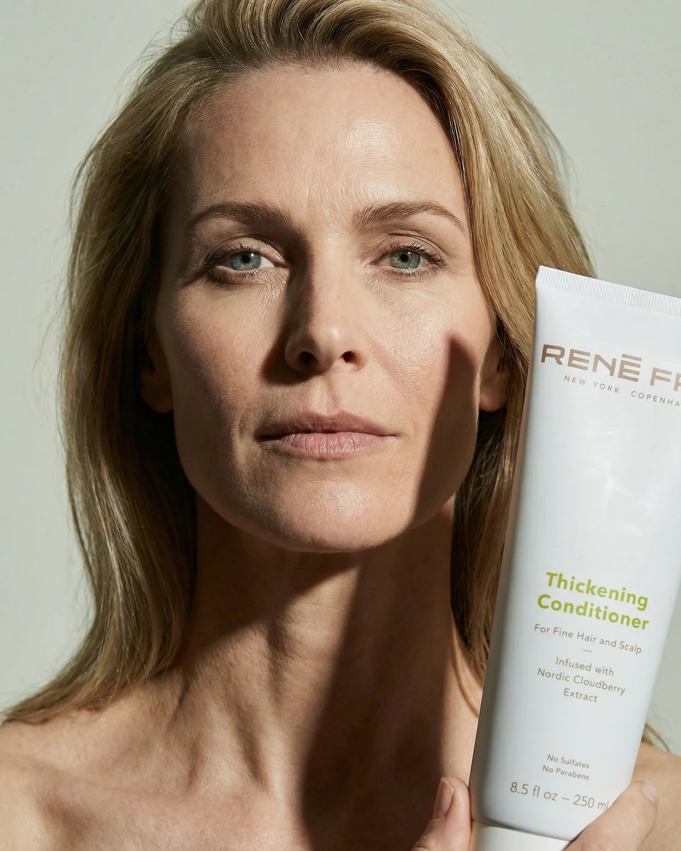 Woman holding a bottle of René Fris Thickening Conditioner against a neutral background
