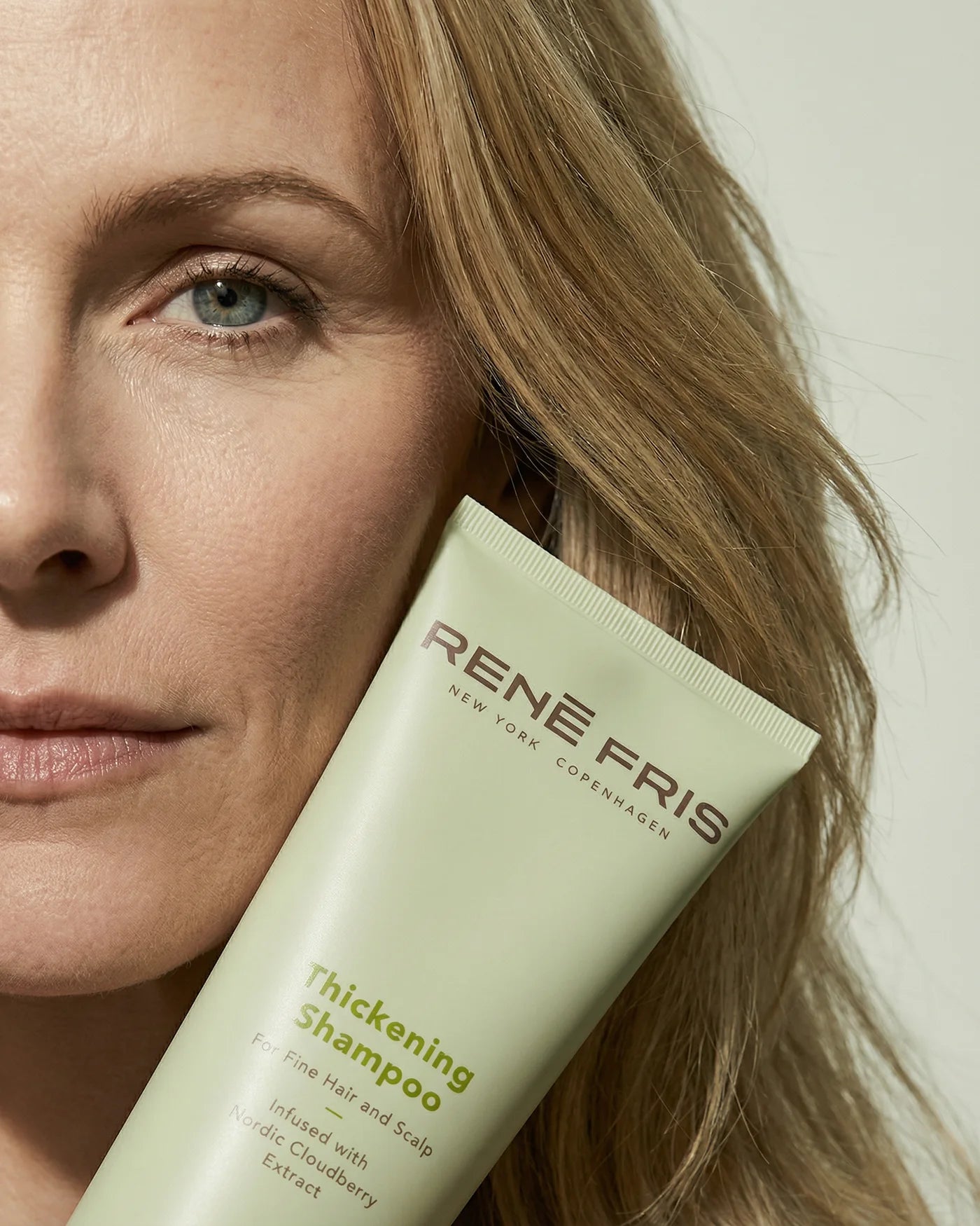 Woman holding a Rene Fris Thickening Shampoo tube close to her face